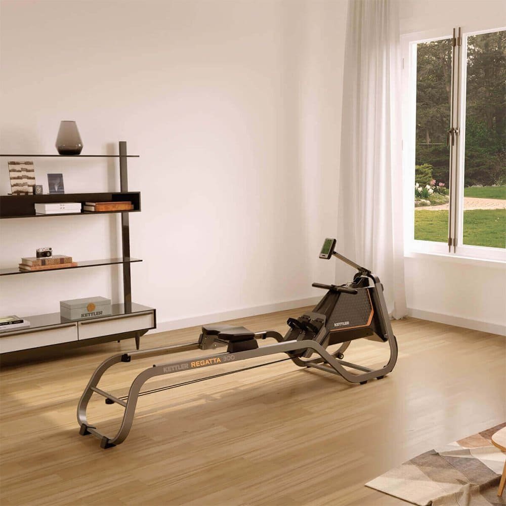 A modern rowing machine set up in a bright, minimalist living room with light wood floors, a shelving unit on the left, and a large window with sheer curtains overlooking a green garden.